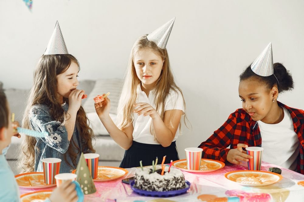 Children wearing party hats gathered around a birthday cake